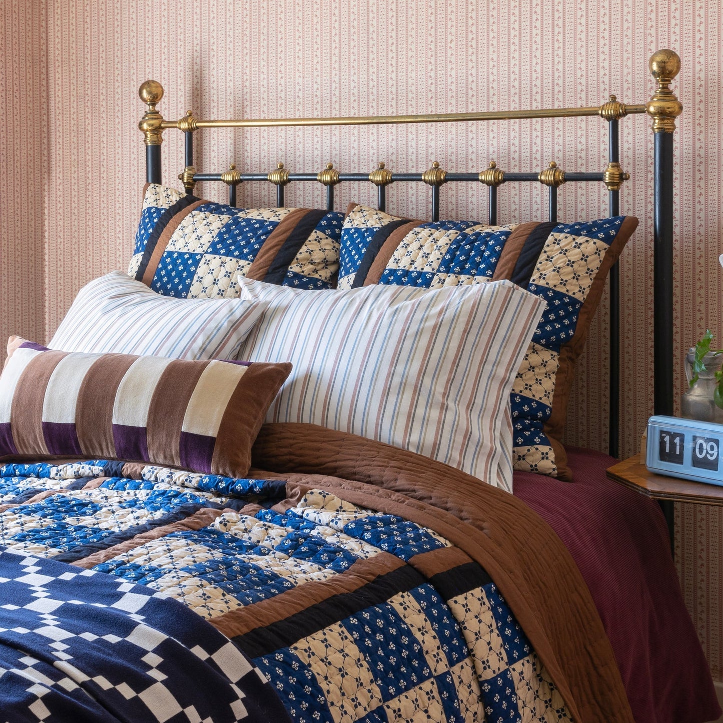 Angled view of Pieced Velvet Pillow Cover showcasing blue-and-cream quilted patchwork and brown velvet stripes on a bed with brass headboard