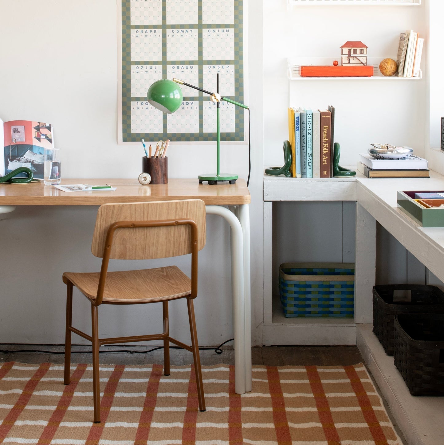 Plaid wool reversible rug under a desk in a bright home office with a wooden stool and green desk lamp