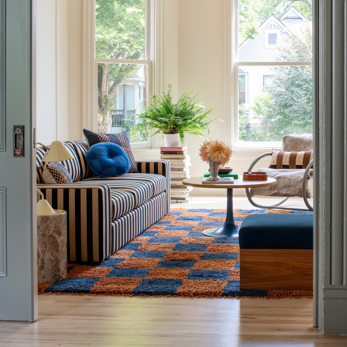 Sunlit living room with the Jacques Shag wool rug in rust and navy checkerboard, striped sofa, and coffee table