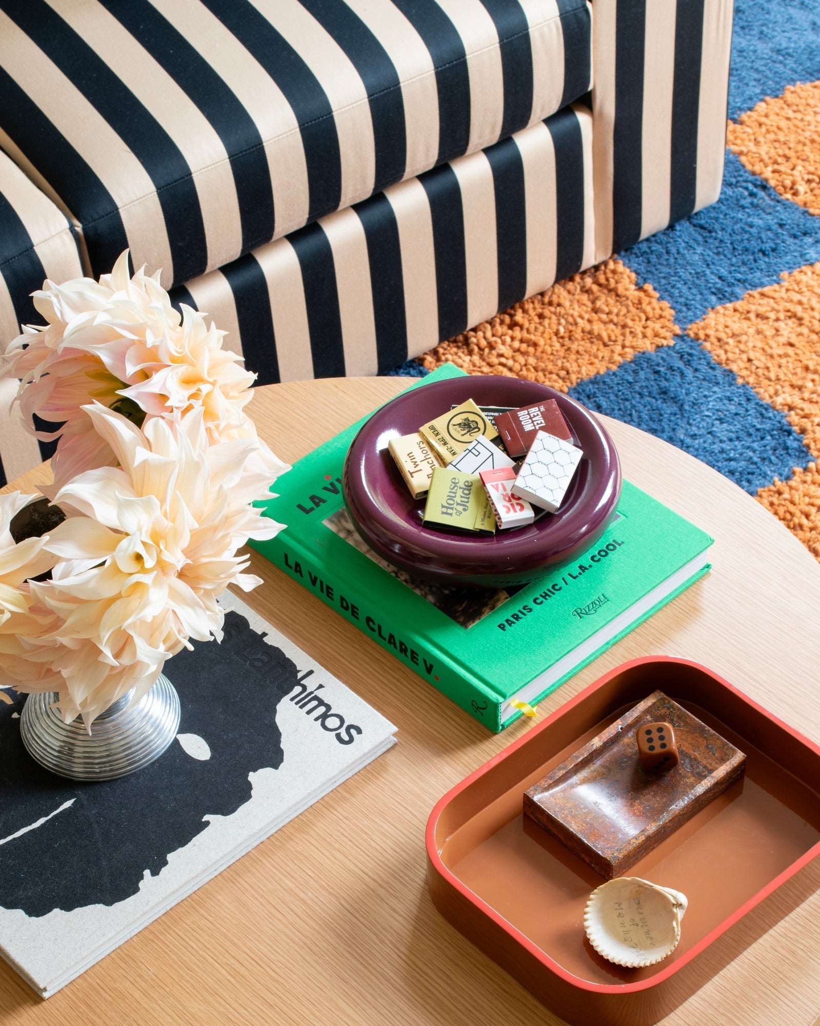 Blue-and-orange checked Jacques Shag Wool Rug under a black-and-cream striped sofa with a styled coffee table and flowers