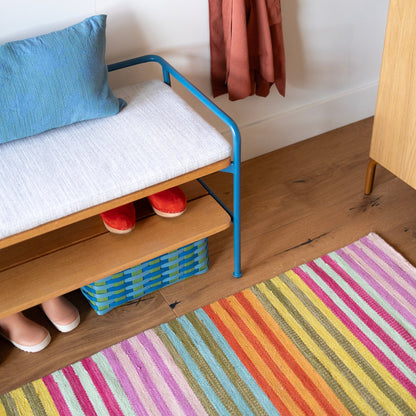 Lisse Performance Rug with narrow multicolor diagonal stripes on hardwood floor, styled with a bench with blue metal frame and cushion