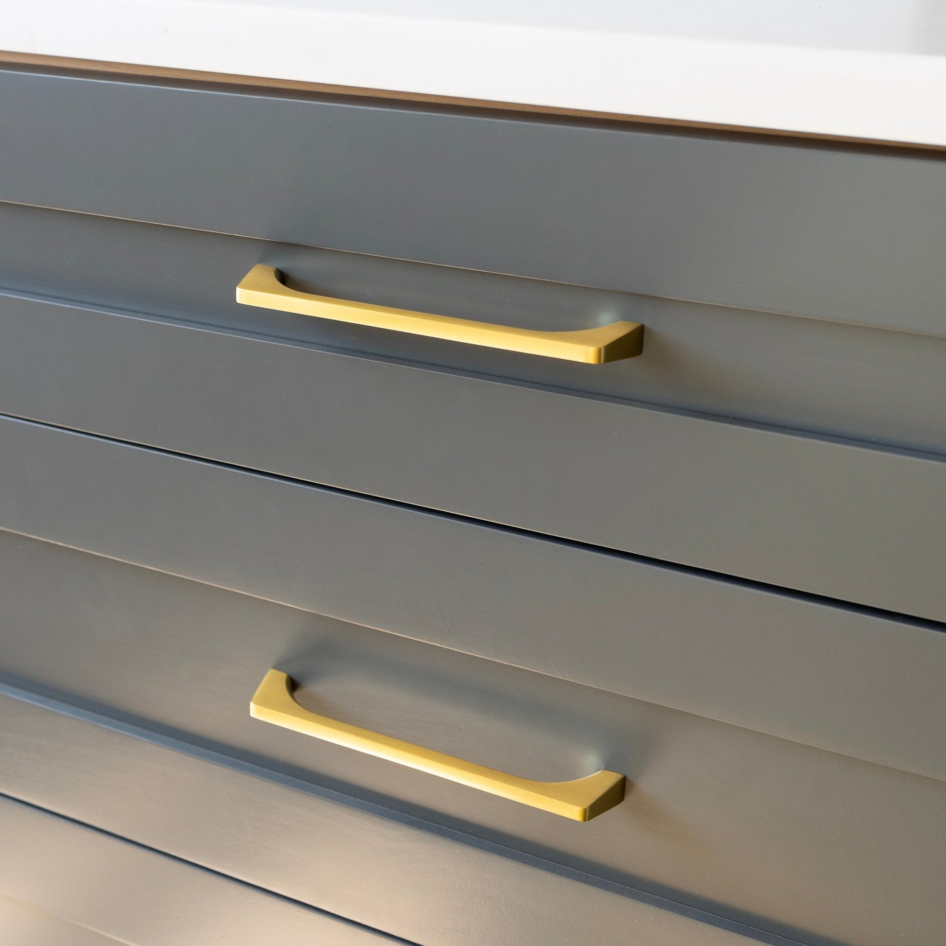 Angled close-up of Truss Pull showing natural brass finish and tapered profile on a dark gray drawer front