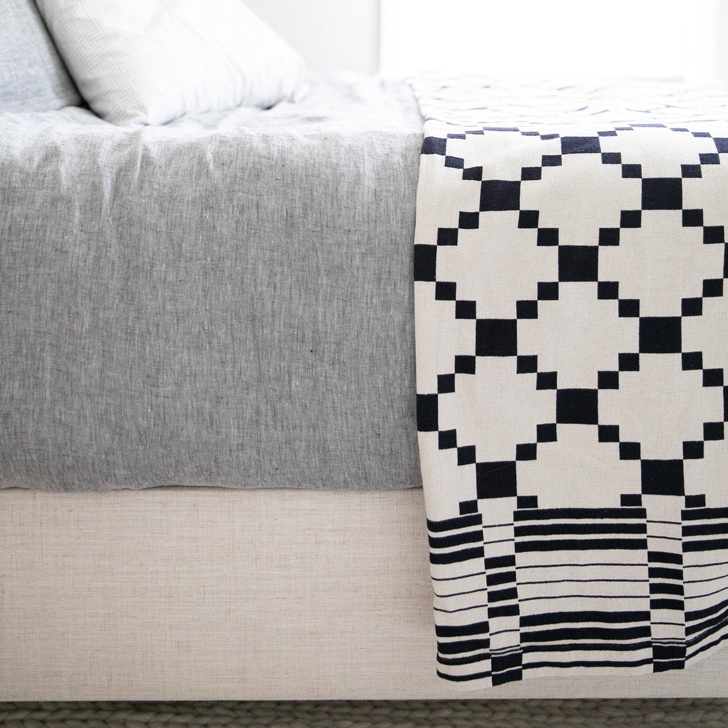 Close-up of Winter + Summer Cotton Coverlet showcasing navy geometric pattern and knit texture with light gray bedding background