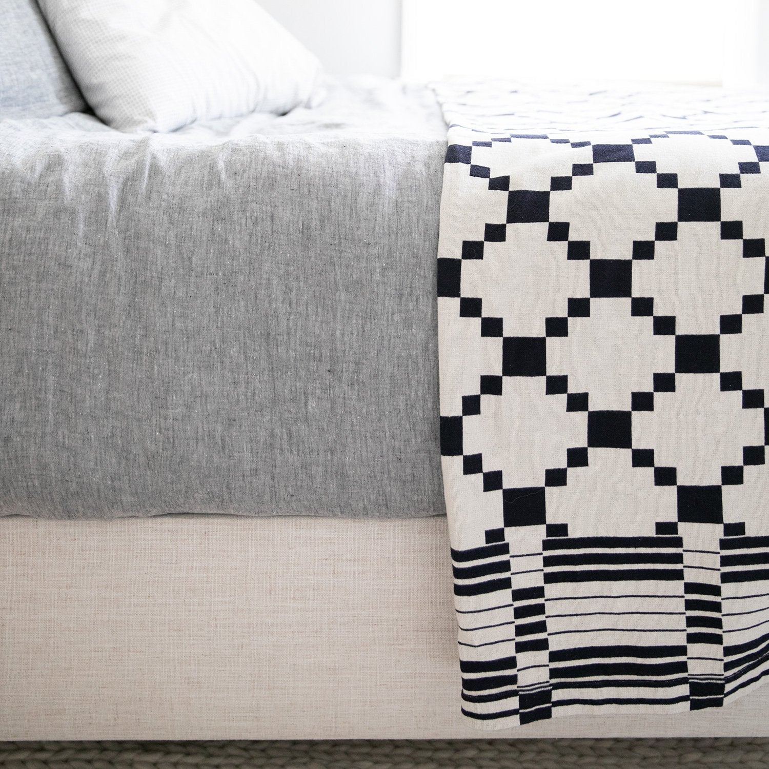 Close-up of Winter + Summer Cotton Coverlet showcasing navy geometric pattern and knit texture with light gray bedding background