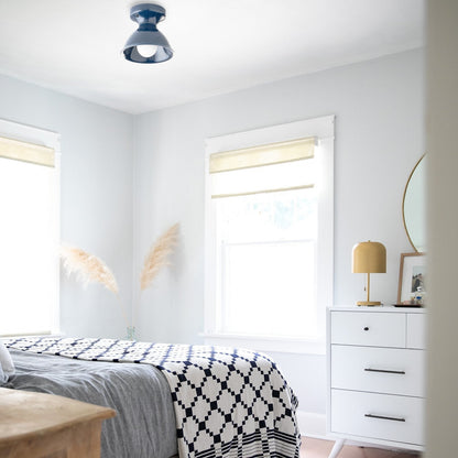 Sunlit bedroom showing a navy-and-white geometric cotton coverlet layered over gray bedding beside a white dresser with a gold lamp