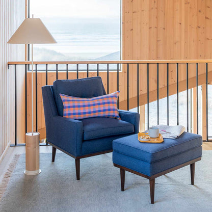 Mesa Wool Rug visible under a navy armchair and ottoman in a wood paneled room with a floor lamp and ocean view window