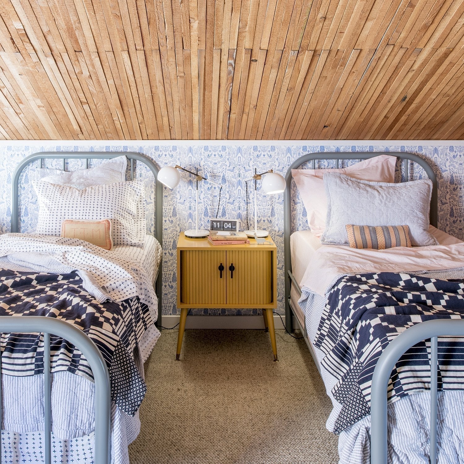 Two twin beds styled with Winter + Summer Cotton Coverlets in navy and white, yellow nightstand between them and slatted wood ceiling above