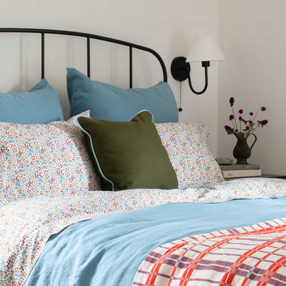 Angled close-up of Wallowa Floral Percale pillowcase set showing small blue and rust floral print on white percale with blue shams and black metal headboard