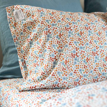 Angled close-up of Wallowa Floral Percale pillowcase showing multicolor floral print on white percale with teal pillow behind