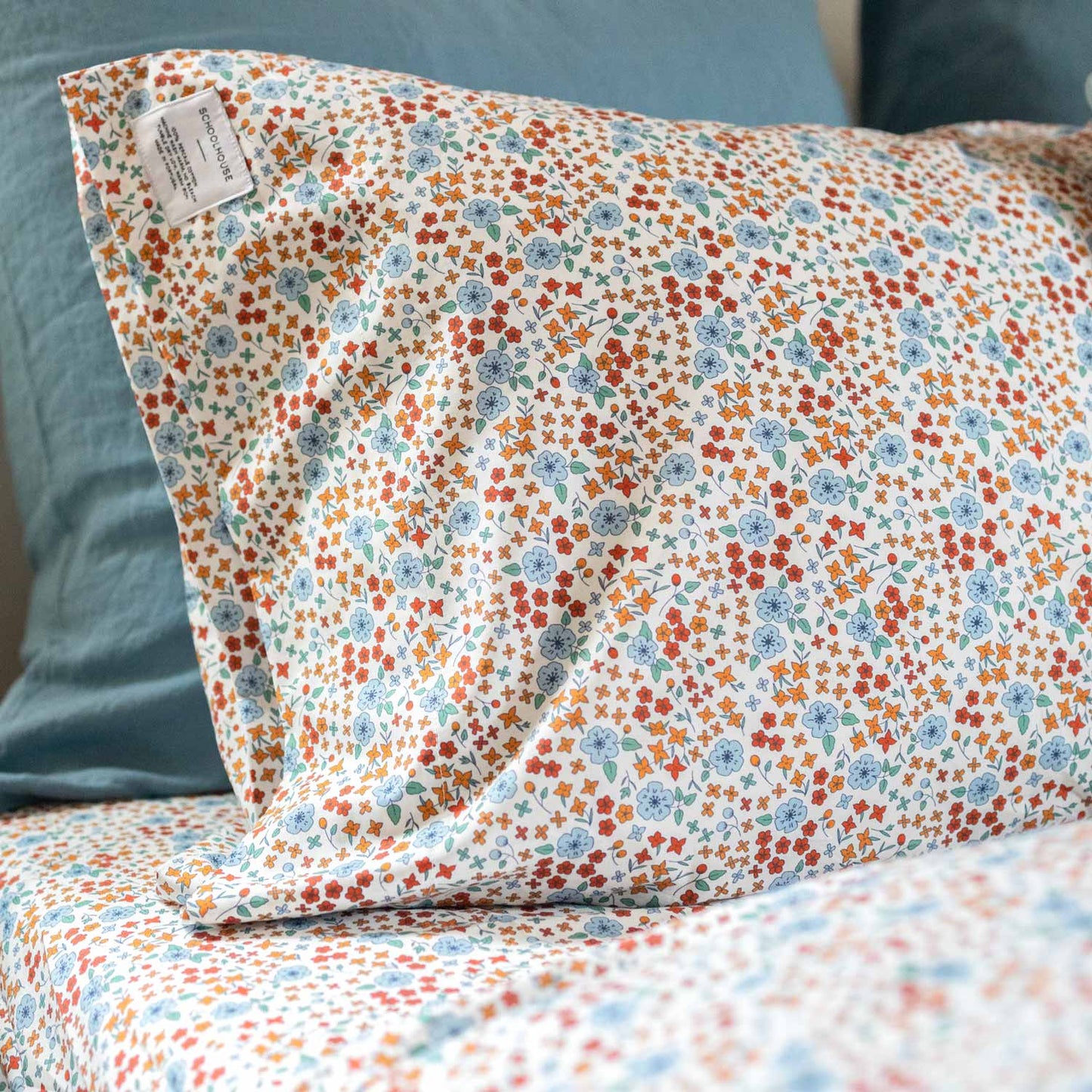 Close-up of Wallowa Floral Percale pillowcase showcasing small orange and blue floral print on white 100% cotton percale with teal pillow background