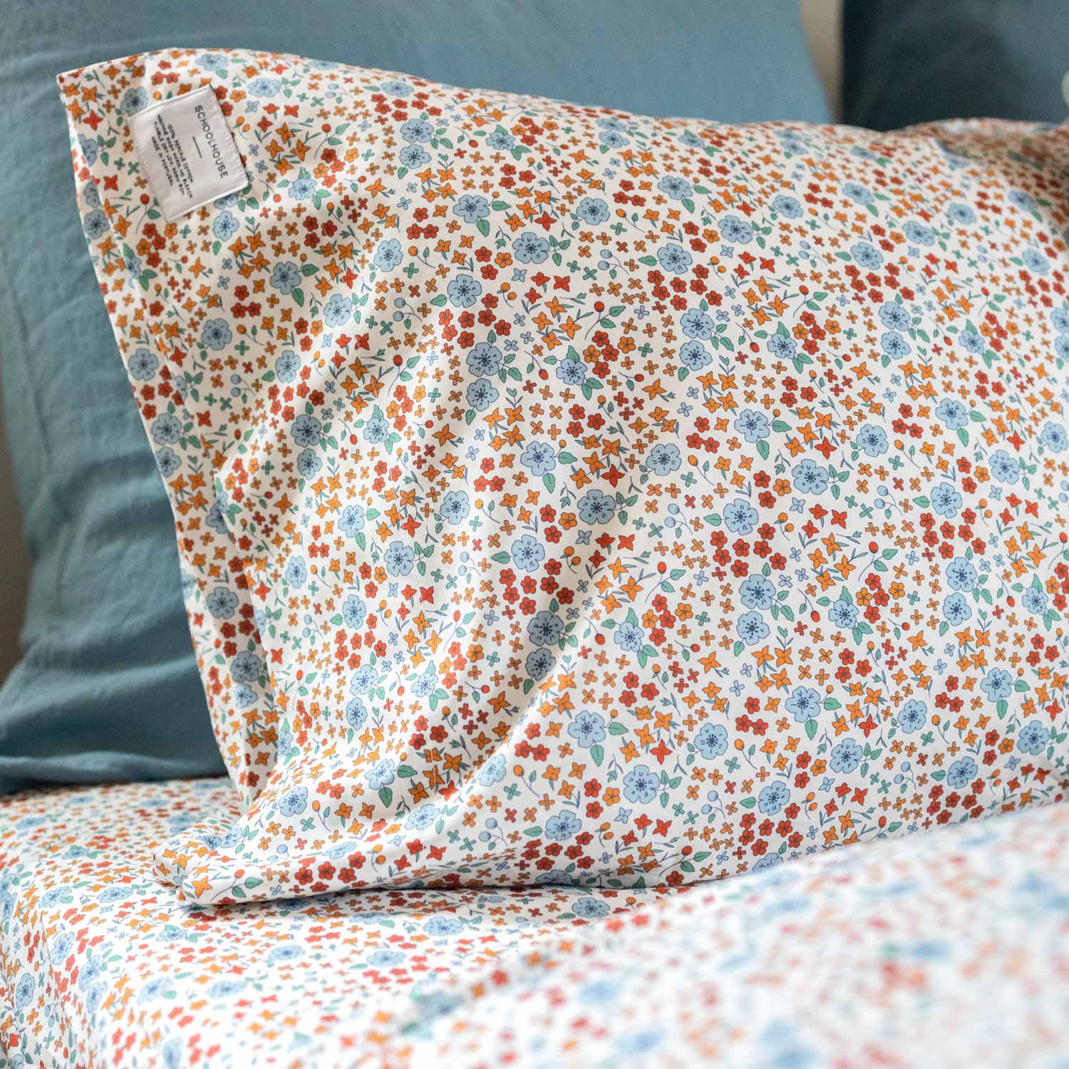 Close-up of Wallowa Floral Percale pillowcase showcasing small orange and blue floral print on white 100% cotton percale with teal pillow background