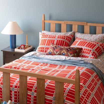 Bedside view of Wallowa Floral percale pillowcases with small blue and brown floral print, styled with red plaid pillows
