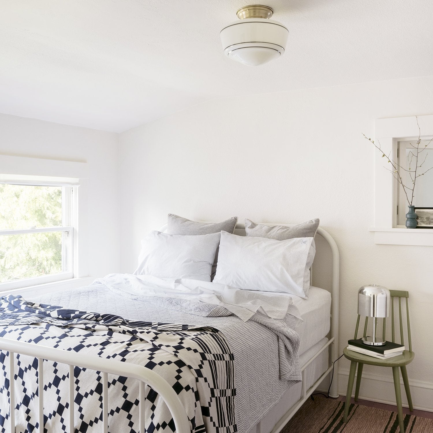 Bed with Winter and Summer Cotton Coverlet in navy and white on a white frame, bright bedroom with green side table and lamp