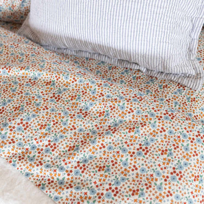 Close-up of Wallowa Floral Percale sheet showing small blue, orange, and rust floral print on white with gray striped pillow