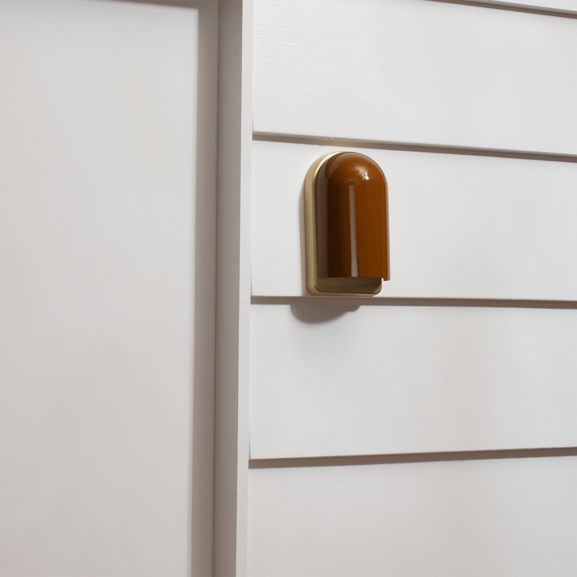 Close-up side view of Allegheny Slim Sconce showing glossy brown rounded shade and brass backplate on white paneled wall