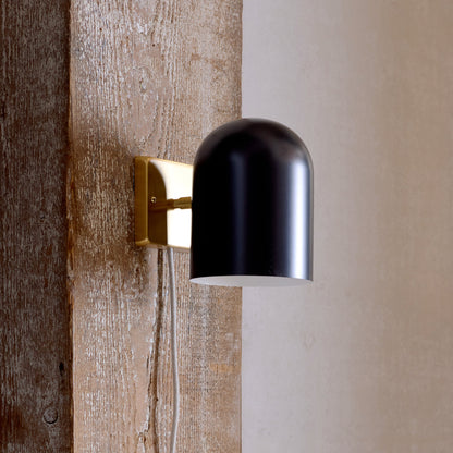 Close-up side view of Allegheny 6-inch plug-in sconce with matte black shade and brass backplate on reclaimed wood
