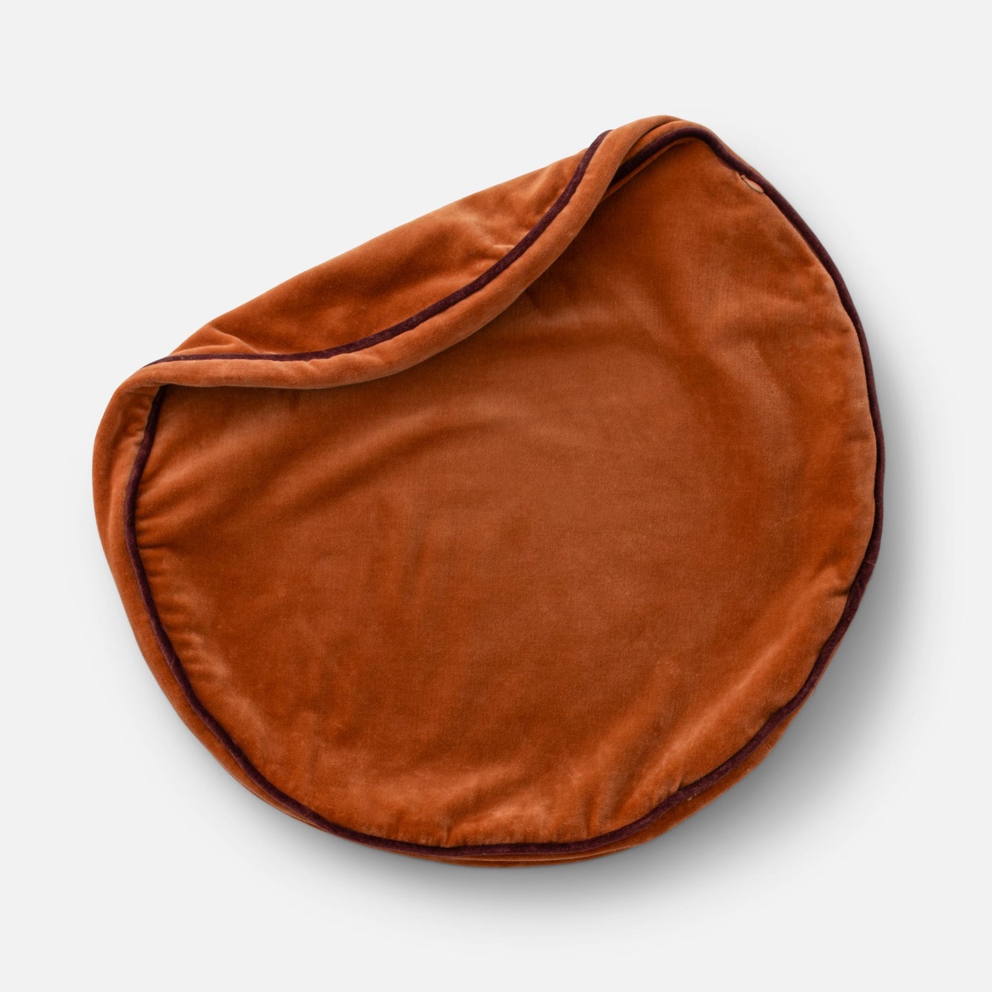 Overhead close-up of Velvet Piped Pillow showing round tawny velvet with dark contrast piping on a light gray background