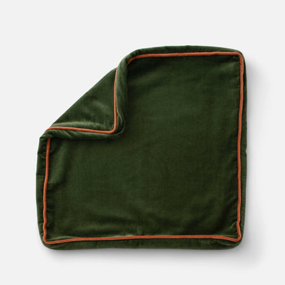 Close-up of Velvet Piped Pillow showcasing deep green cotton velvet and rust contrast piping on a light gray background