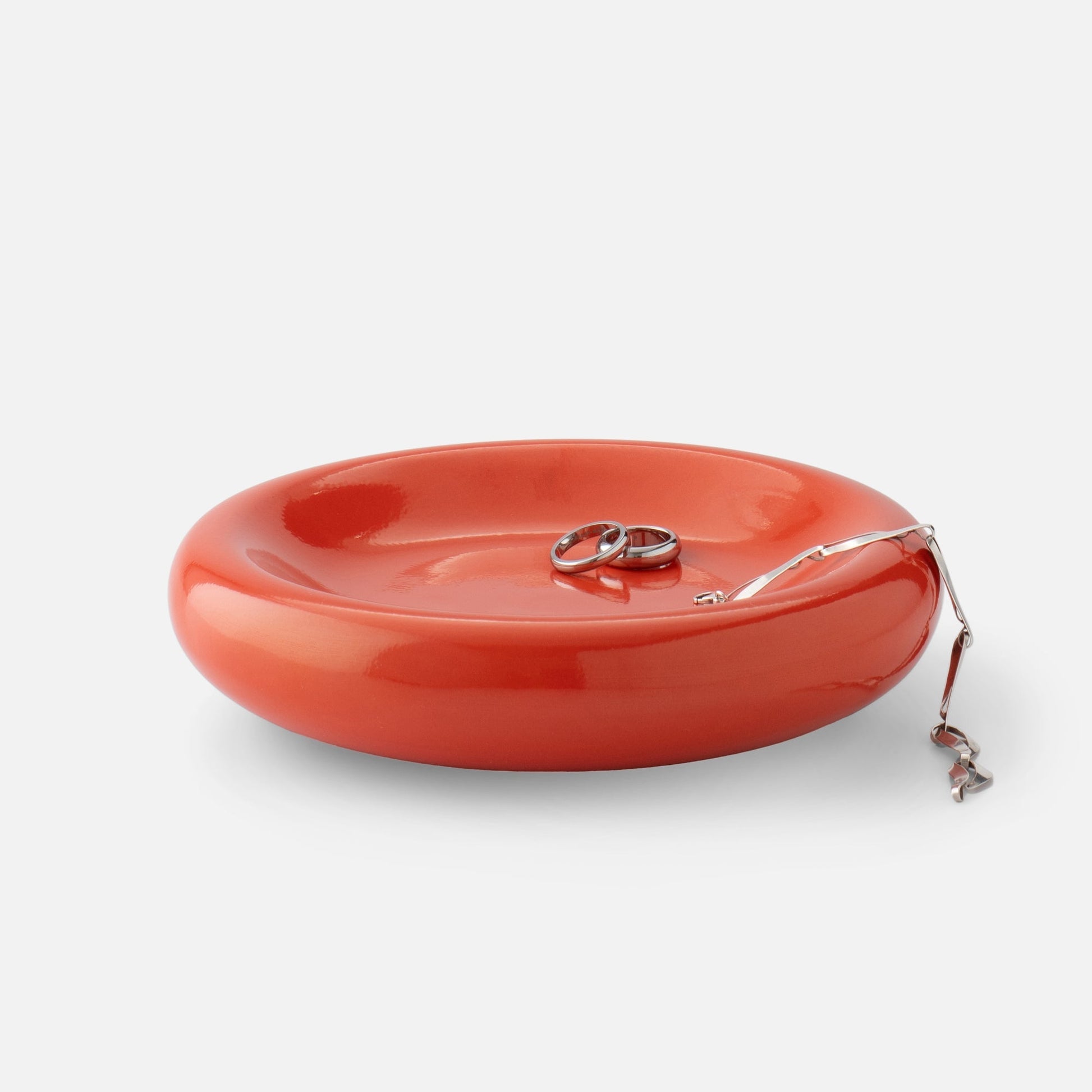 Close-up top view of Yves cast metal catch-all in Raisin Gloss showing stacked rings and a chain on white background