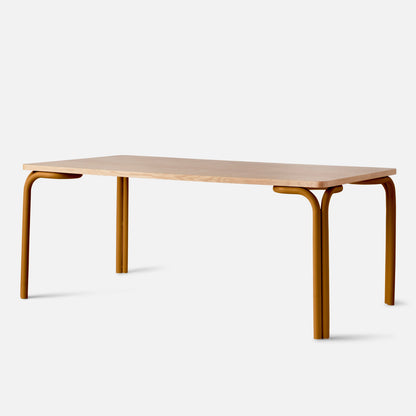Three-quarter view of Forma dining table showing light oak rectangular top and rounded mustard metal legs on white background