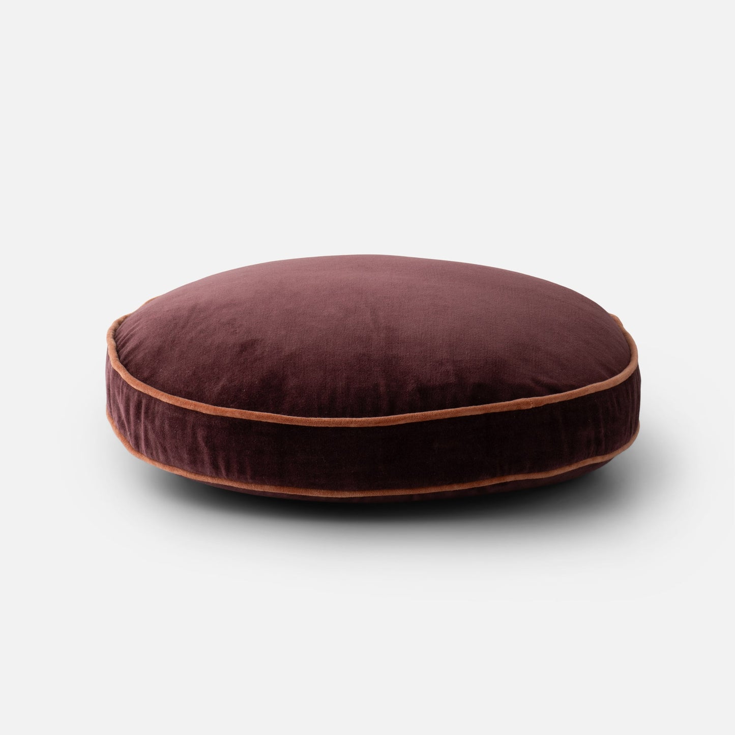 Low front view of Velvet Piped Pillow showcasing raisin cotton velvet and rust piped edge on light gray background