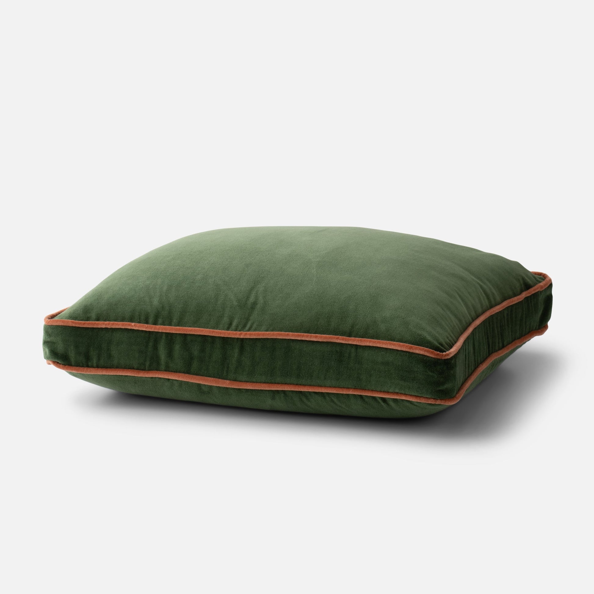 Angled close-up of Velvet Piped Pillow showcasing green cotton velvet and rust contrast piping on a light gray background