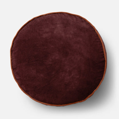 Overhead view of Velvet Piped Pillow showcasing round shape, raisin velvet fabric, and rust piped edge on light gray background