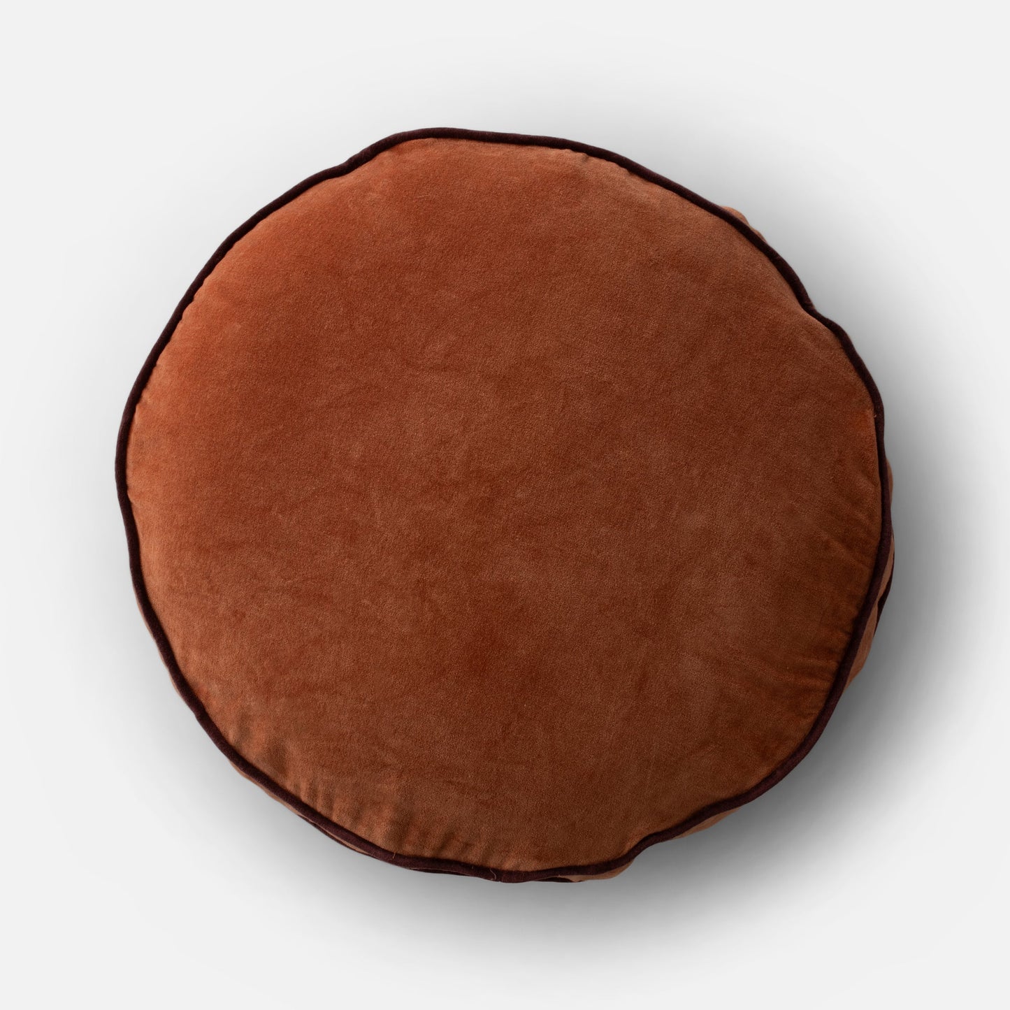 Overhead view of Velvet Piped Pillow showing round shape, tawny cotton velvet and dark contrast piping on light gray background