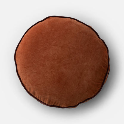 Overhead view of Velvet Piped Pillow showing round shape, tawny cotton velvet and dark contrast piping on light gray background