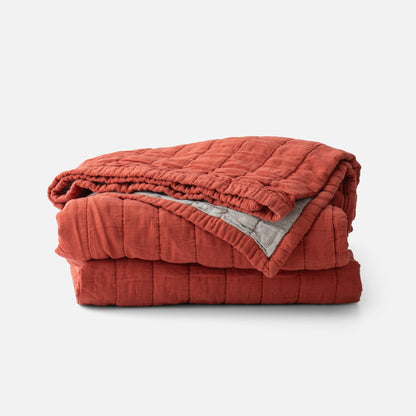 Front view of Channeled Cotton Quilt folded to show red channeled quilting and gray striped reverse on white background