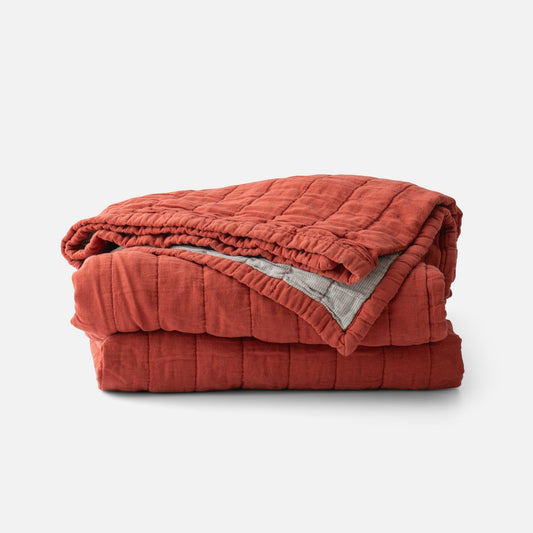 Front view of Channeled Cotton Quilt folded to show red channeled quilting and gray striped reverse on white background