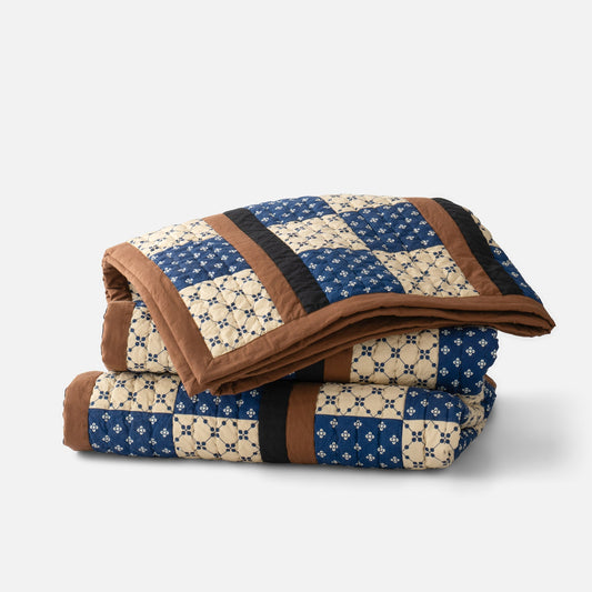 Folded Albright Pieced Quilt showcasing blue and cream patchwork squares with brown trim on white background