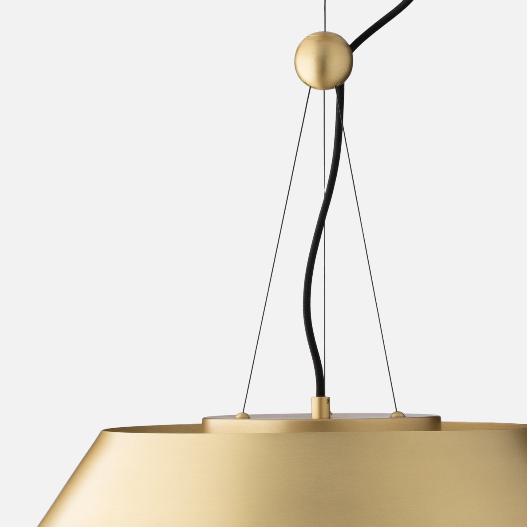 Close-up of Alfred Pendant showing natural brass shade rim, top canopy, and black cord and support cables against a light gray background