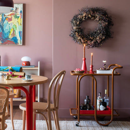 Three-quarter view of Lolly Bar Cart showcasing bent steel frame, tempered glass shelves, and ball casters against a pink dining room wall