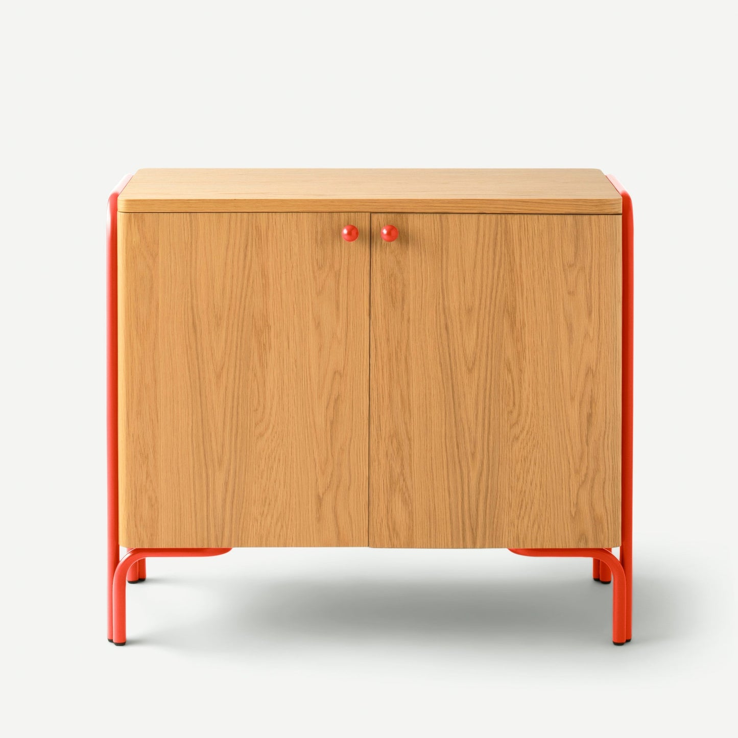 Front view of Forma cabinet showing oak veneer double doors with red knobs and red metal frame and legs on white background