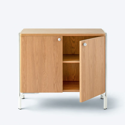 Front view of Forma Cabinet in persimmon oak veneer, one door ajar revealing adjustable shelf, white powder-coated legs