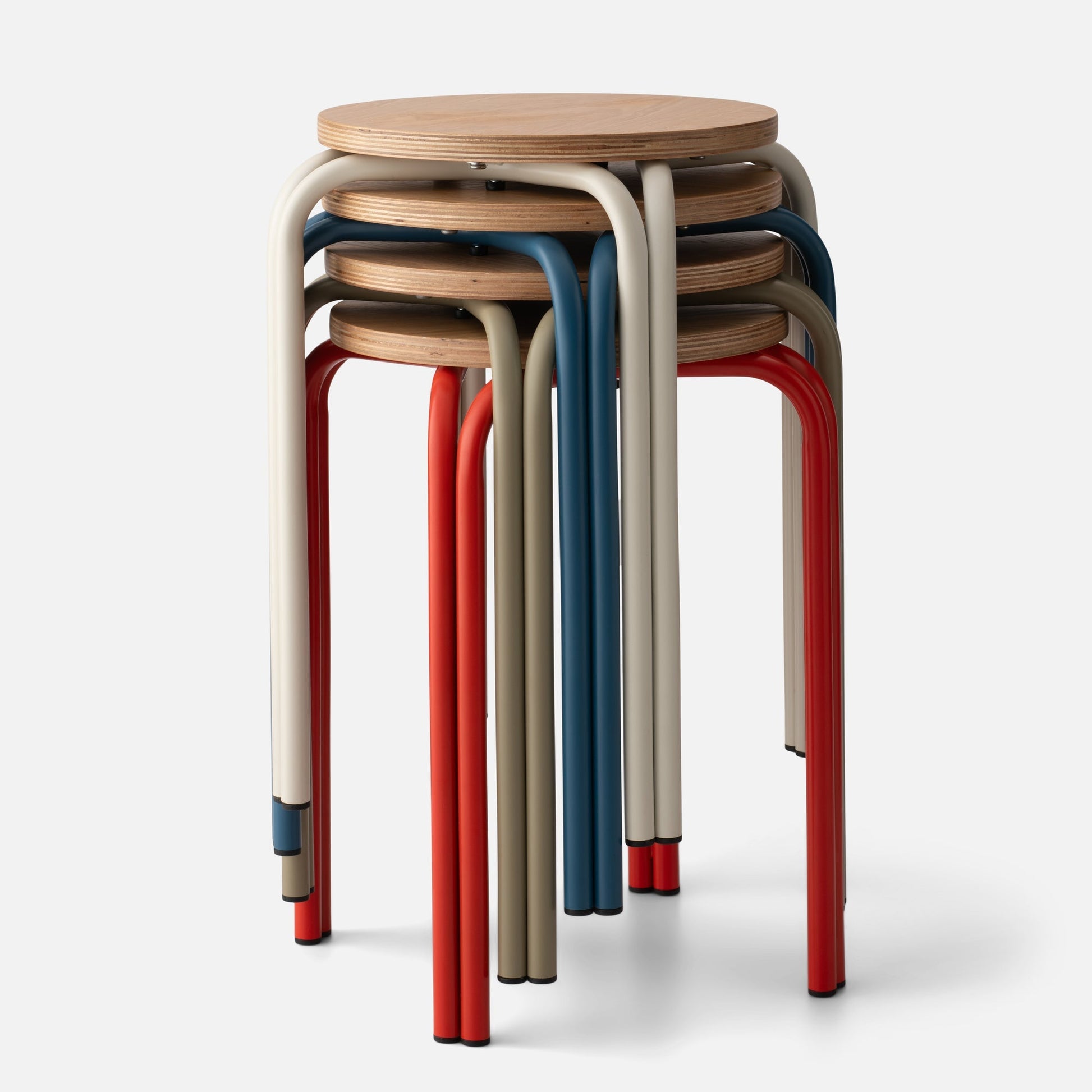 Close-up front view of stacked Forma Stool showcasing oak plywood tops and powder coated steel legs in red, indigo, shell white, and lichen on a light background