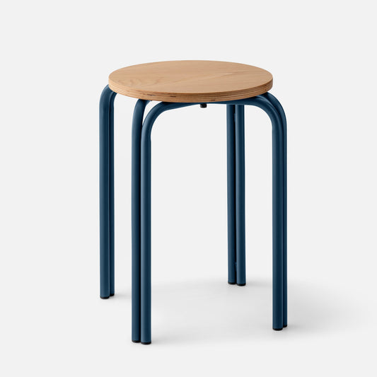 Three-quarter view of Forma Stool showing round white oak top with exposed plywood edge and indigo powder-coated steel legs on light gray background