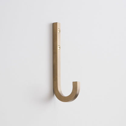 Angled view of J Hook in natural brass showing square solid-brass profile and two visible mounting screws on white wall