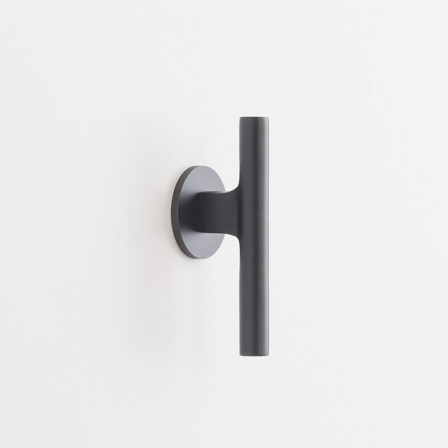Side view of Galley Pull showing matte black cylindrical bar and round backplate on a white wall