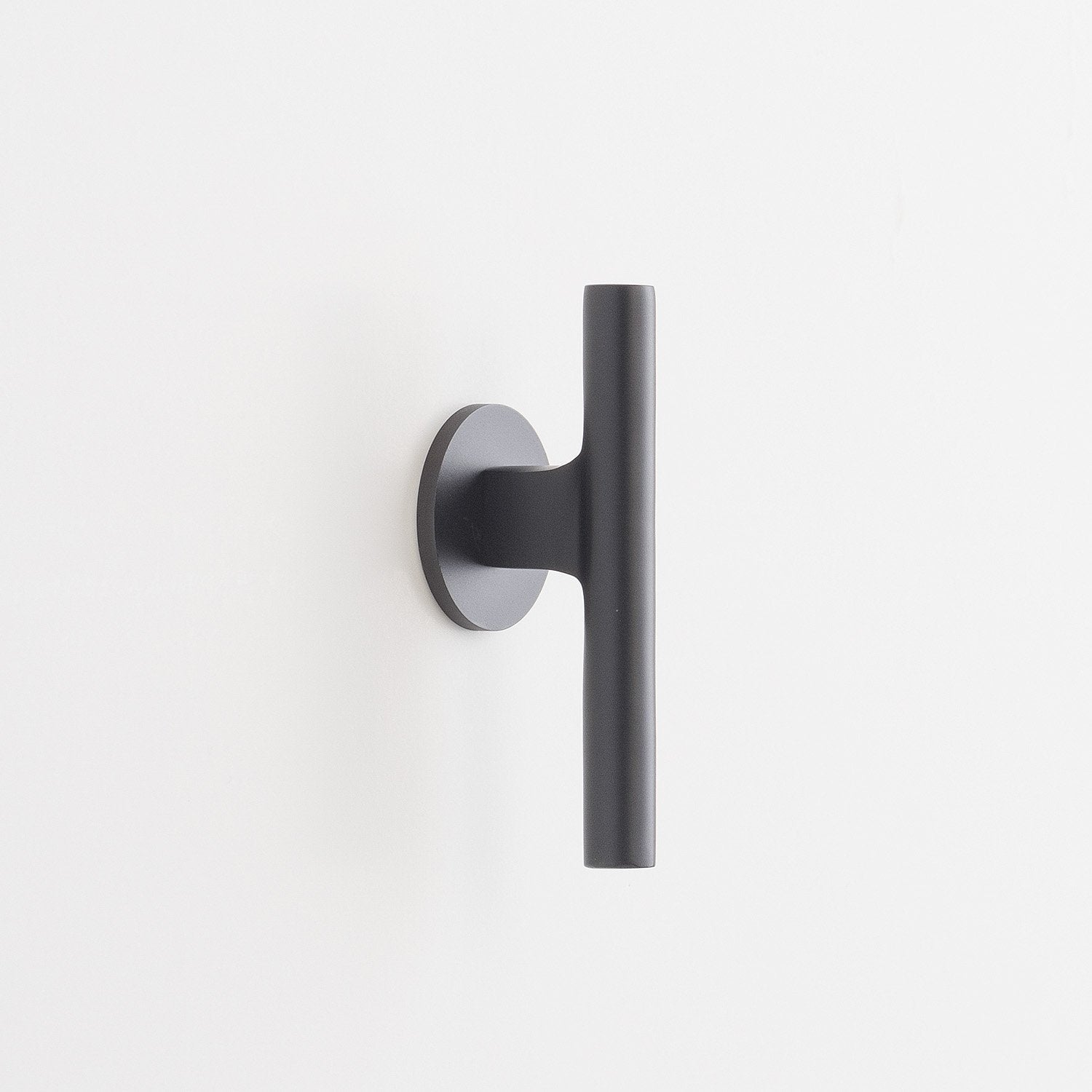 Side view of Galley Pull showing matte black cylindrical bar and round backplate on a white wall