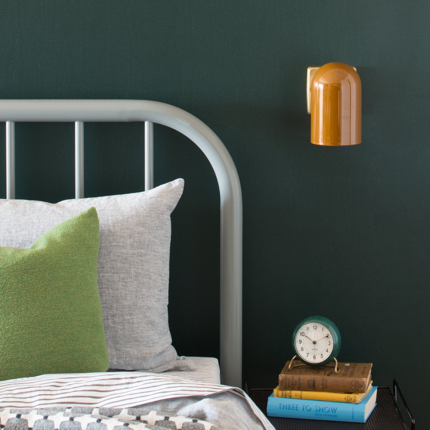 Allegheny 4.5-inch sconce mounted on a dark green wall above a bedside table next to a gray metal bedframe