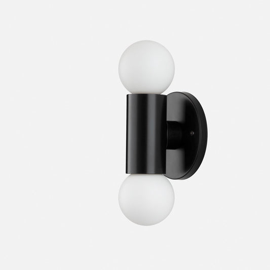Side view of Cylinder Double Sconce showcasing matte black cylindrical body with two white glass globe bulbs and round wall plate on light gray background