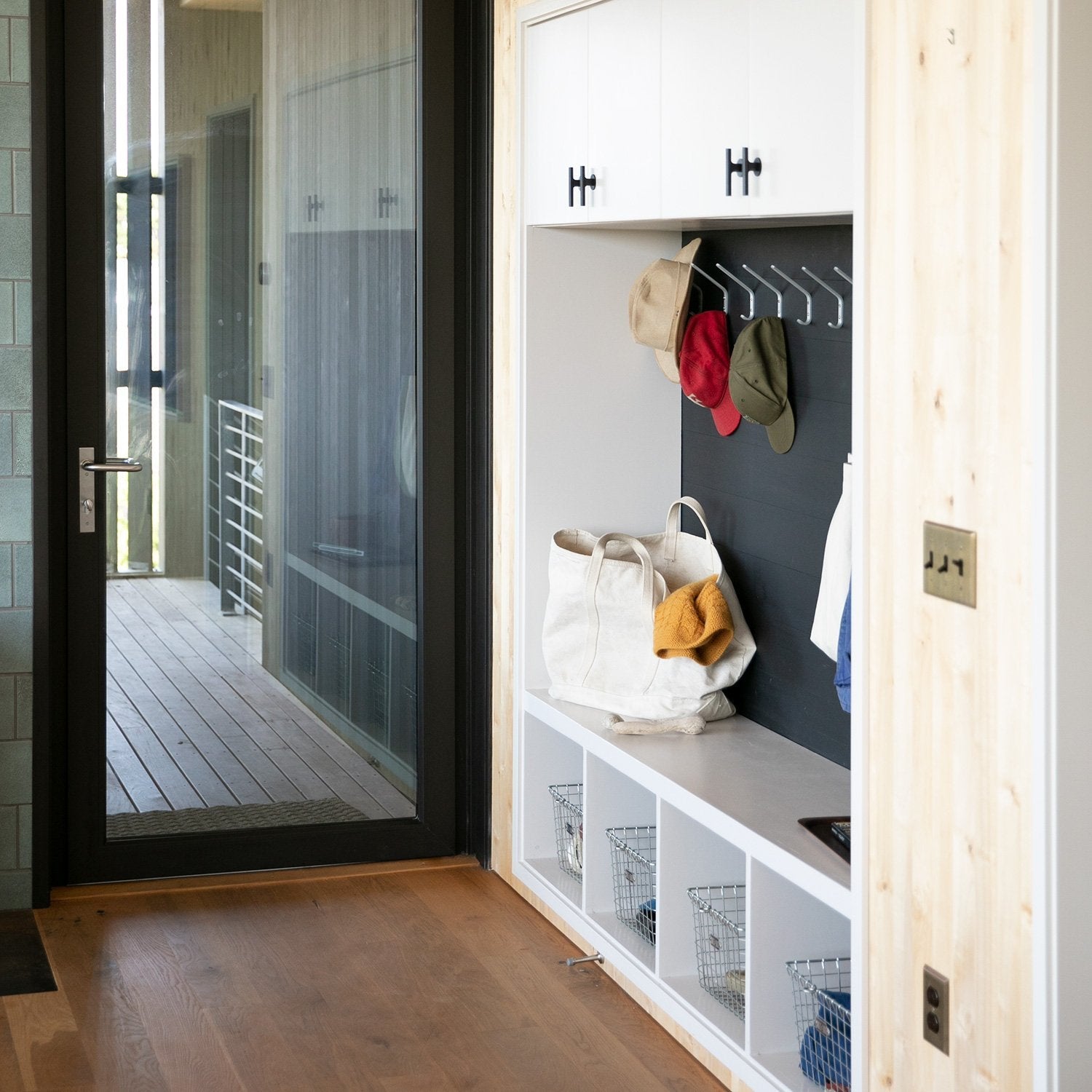Entryway storage showcasing black Galley Pull cabinet pulls mounted on white cabinets, canvas tote on bench and hats hanging on hooks