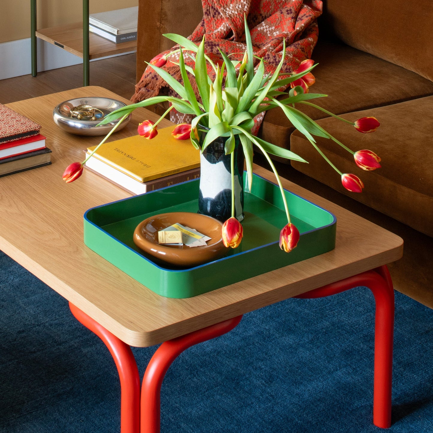 Angled close-up of Yves cast metal catch-all with polished silver finish on a wood table beside books and red tulips