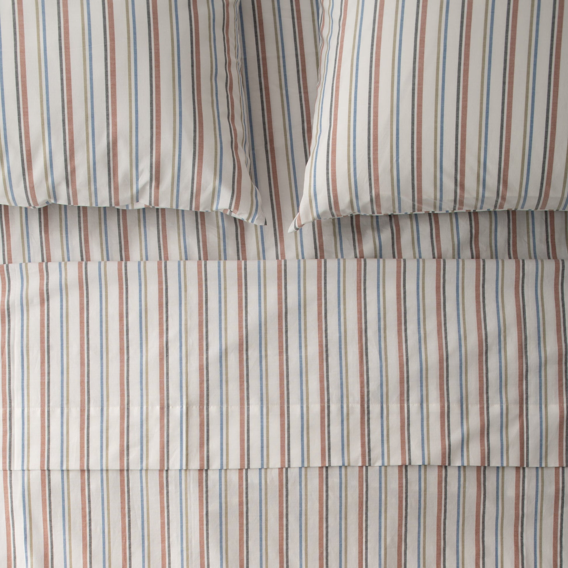 Top-down view of Fresh Stripe percale sheeting showcasing narrow blue and rust vertical stripes with two pillowcases on a flat bed