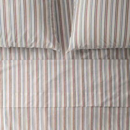 Top-down view of Fresh Stripe percale sheeting showcasing narrow blue and rust vertical stripes with two pillowcases on a flat bed