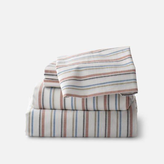Stacked Fresh Stripe Percale sheeting showcasing tawny, olive, indigo, and black yarn-dyed stripes on a soft gray background
