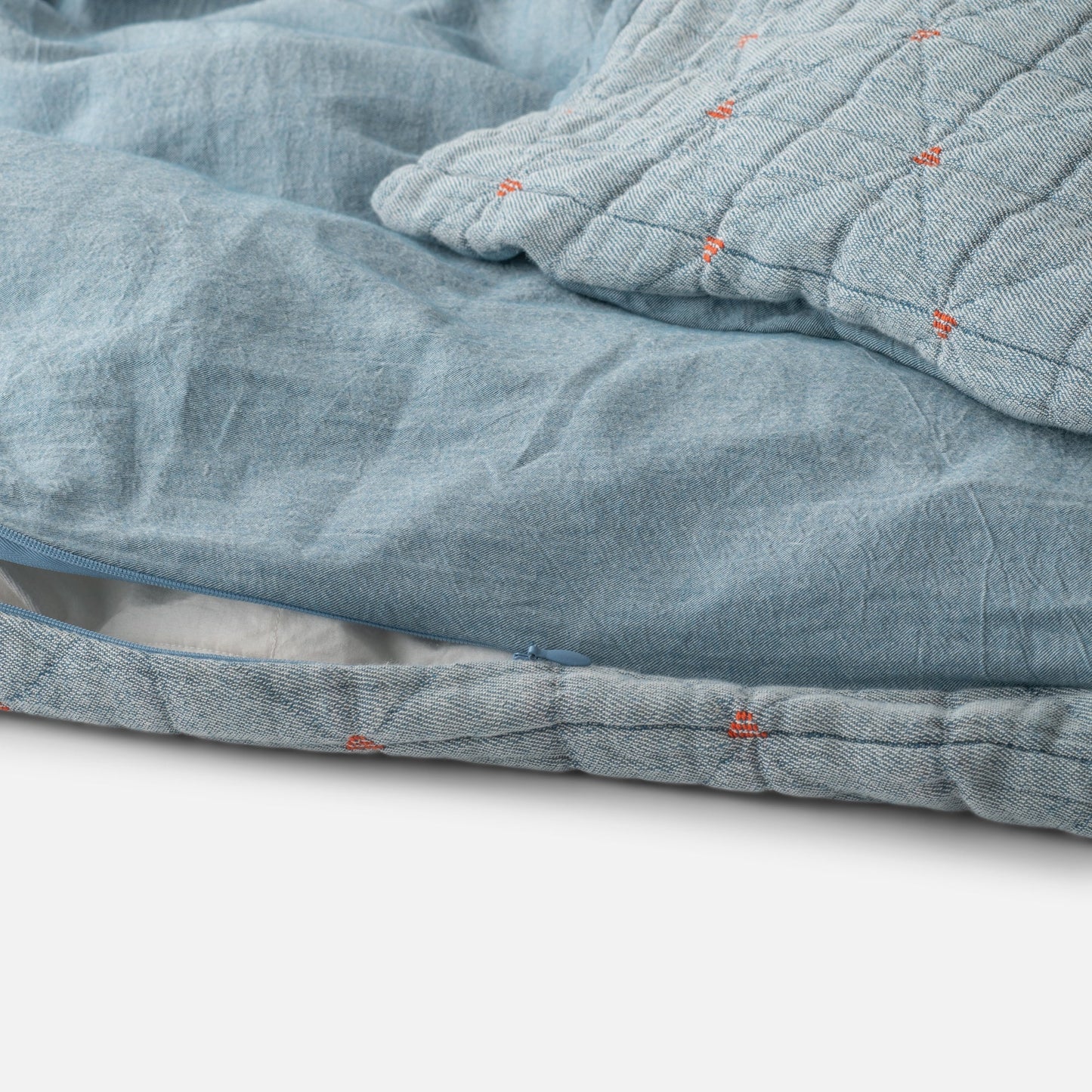 Close-up of Peak Stitch Duvet showcasing triangular quilting, red yarn-tie stitching, and hidden zipper on blue matelassé fabric