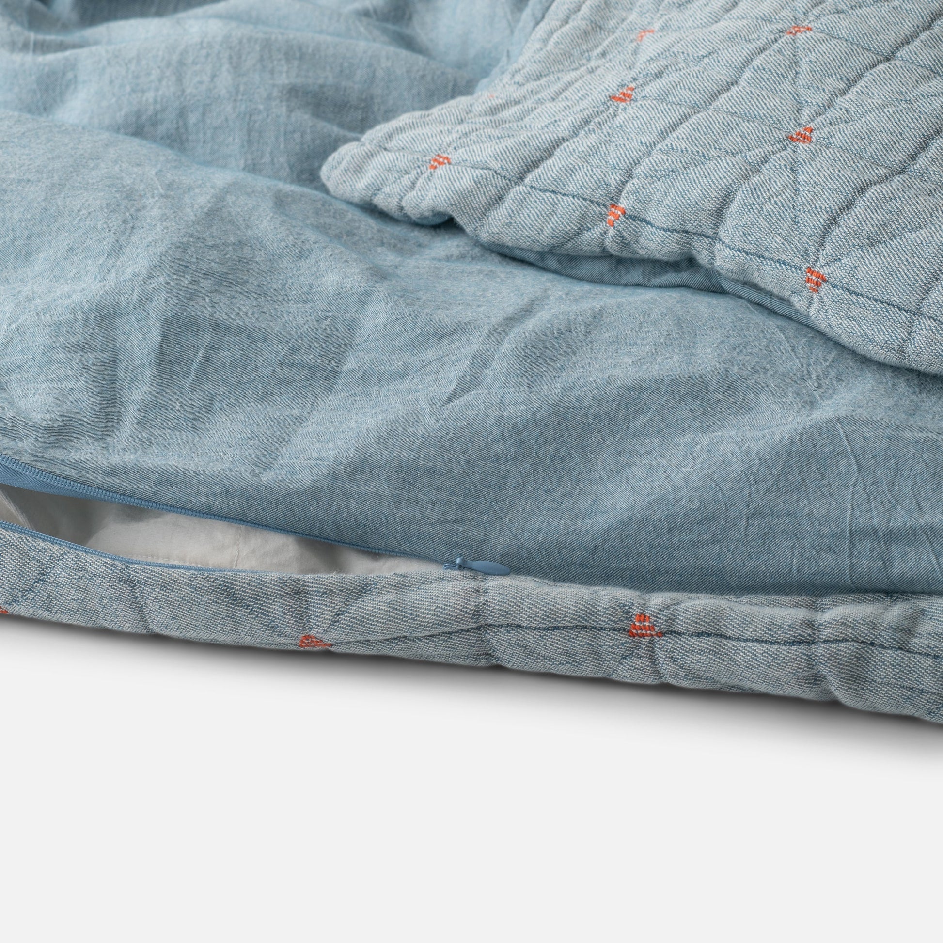 Close-up of Peak Stitch Duvet showcasing triangular quilting, red yarn-tie stitching, and hidden zipper on blue matelassé fabric